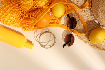 String bag with sunglasses, fruits and summer accessories on beige background, flat lay. Space for...