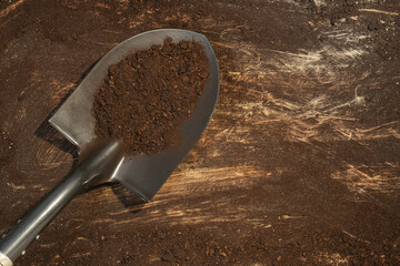 Metal shovel with fertile soil on dirty wooden surface, top view. Space for text