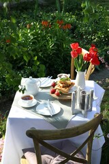 Beautiful bouquet of tulips and freshly baked waffles on table served for tea drinking in garden