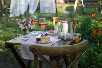 Vase with spring flowers, wine and cake on table served for romantic date in garden