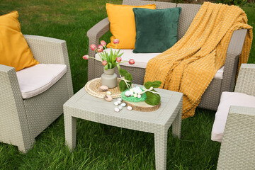 Easter decorations. Bouquet of tulips in vase, bunny figures and decorated eggs on table in backyard