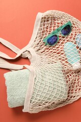 String bag, sunglasses, cosmetic product and towel on coral background, top view