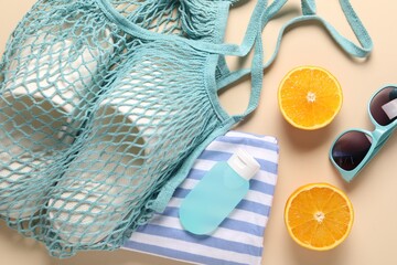 String bag, different beach accessories and orange on beige background, flat lay