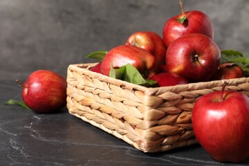 Fresh red apples and leaves in basket on dark grey table, closeup