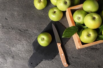 Ripe green apples with water drops, cutting board and knife on grey table, flat lay. Space for text