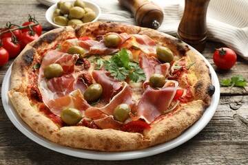 Tasty pizza with cured ham, olives, tomatoes and parsley on wooden table