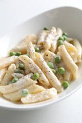 Delicious pasta with green peas and creamy sauce in bowl on white table