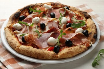 Tasty pizza with cured ham, olives, mozzarella cheese, sun-dried tomato and arugula on table,...