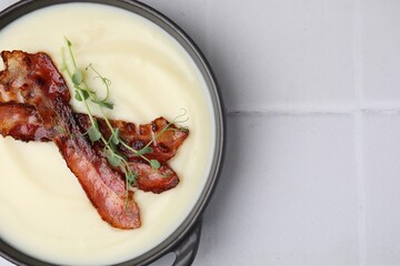 Delicious potato soup with bacon and microgreens in bowl on white tiled table, top view. Space for text