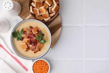 Delicious lentil soup with bacon and parsley in bowl on white tiled table, flat lay. Space for text