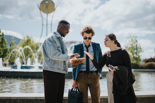 Three mixed race business professionals engaging in a discussion outdoors. They are reviewing data on a tablet, brainstorming solutions, and strategizing for growth.