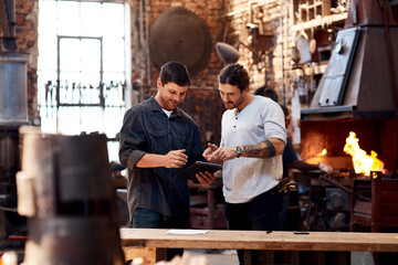 Men, blacksmith and tablet in workshop on teamwork for research and collaboration. Small business, craft and metal with browsing internet for steel ideas, engineer and manufacturing as welder