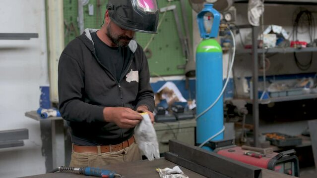 Safety at work: a blacksmith, before welding, wears a protective mask and work gloves. He positions the welding machine on the point to be welded and activates it, creating glare, sparks and smoke.