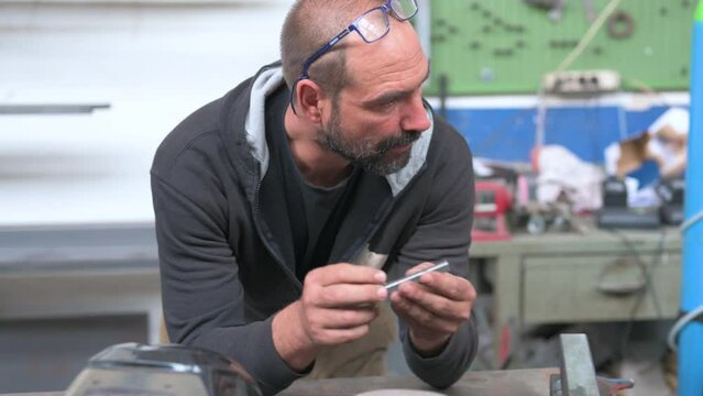 A blacksmith reflects on the realization of a job: he analyzes a metal bar until he thinks he has found the solution. He heads towards the tool bench. Solution thinking concept.