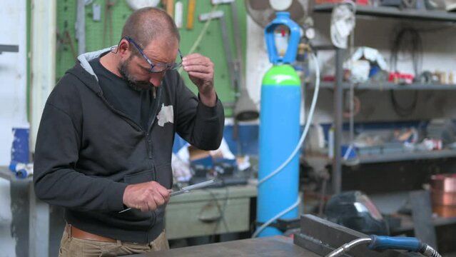 Conceptual metal work footage: Blacksmith is taking measurements of a metal bar with the use of caliper. He then places the piece on the workbench where there is another piece.