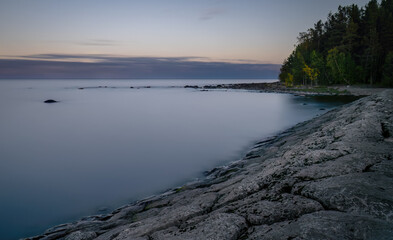 The rocky shore of the lake against the background of sunset and forest. Karelia, Russia.