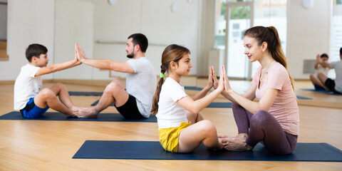 Kids and parents sitting on mats in lotus pose and touching each other palms during family yoga...