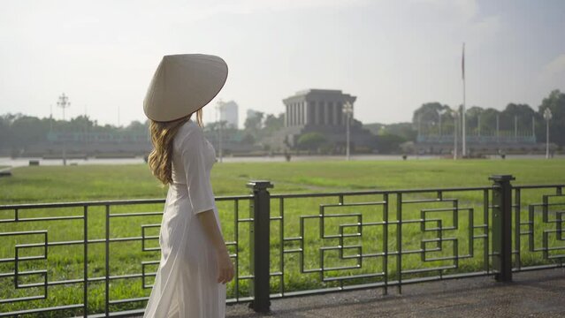 Portrait of Asian Vietnamese woman with Vietnam dress and straw hat travel at Ho Chi Minh Mausoleum, Tourist attraction landmark in urban city town of Hanoi, Vietnam. People lifestyle.