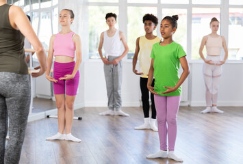 Thin adolescent female attendee of ballet classes training first position together with other group...