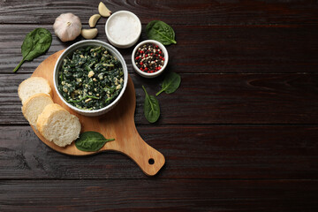 Tasty spinach dip with egg in bowl, spices and bread on wooden table, top view. Space for text