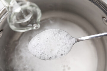 Pouring vinegar into spoon with baking soda over saucepan, closeup