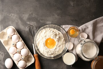 Making dough. Flour with egg yolk in bowl and other products on grey textured table, flat lay