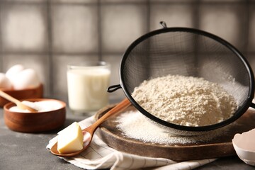 Making dough. Flour in sieve, spoon and butter on grey table, closeup