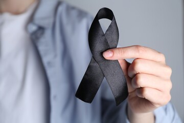 Woman holding black awareness ribbon on grey background, closeup