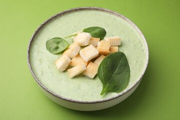 Delicious spinach cream soup with leaves and croutons in bowl on green background