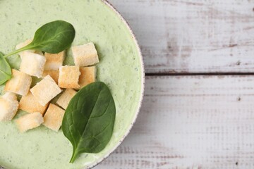 Delicious spinach cream soup with leaves and croutons in bowl on white wooden table, top view. Space for text