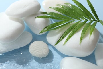 Spa stones and palm leaf in water on light blue background, closeup