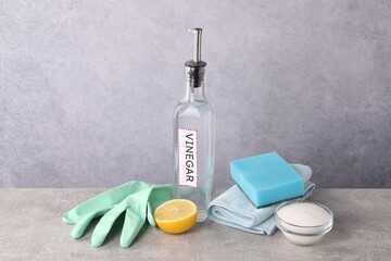 Natural cleaning products. Vinegar in bottle, baking soda, lemon, glove and sponge on light grey...