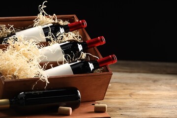 Box with wine bottles on wooden table against black background. Space for text