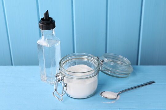 Natural cleaning products. Vinegar in bottle, baking soda and spoon on light blue wooden table
