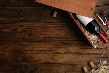 Box with wine bottle, corkscrew and corks on wooden table, flat lay. Space for text