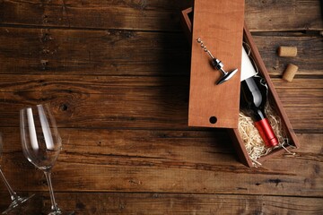 Box with wine bottle, glasses, corkscrew and corks on wooden table, flat lay