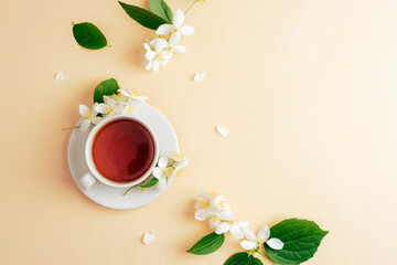 A cup of tea and jasmine flowers on beige background. Top view, flat lay, copy space