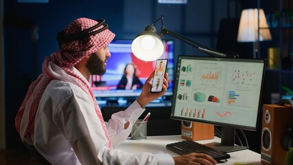 Muslim teleworker and coworkers in call crosschecking analytics statistical data sets in dimly lit...