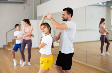 Active teen girl practicing vigorous boogie-woogie in pair with her sporty young father in dance studio during family class