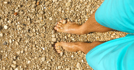 POV: A young man looking down at his bare feet while standing on a pebble shore. Relaxing walk and...