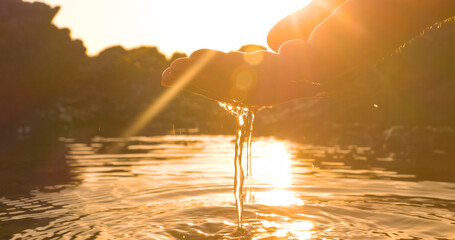 CLOSE UP, LENS FLARE, DOF: Silhouette of a hand gently scooping water from a sea puddle during low...