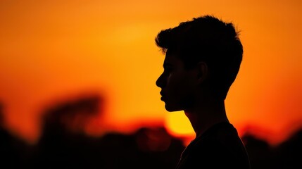 Silhouette of a young man against an orange sunset backdrop