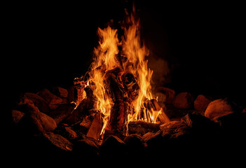 A bonfire with firewood at night on a black background. A close-up photo of the flame.