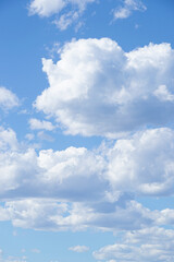 Obraz premium Vertical photograph of a blue sky with many clouds of various shapes and textures.