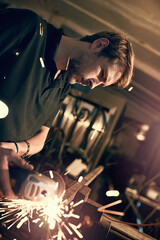 Handy man, sparks and angle grinder with welder at night in workshop for repair and maintenance. Home renovation, creativity and construction worker or carpenter with project for small business