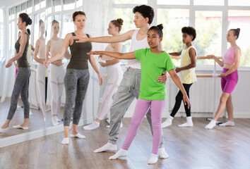 Focused African American teenage girl carefully practicing ballet moves and basic lifts paired with boy in children dance studio run by female instructor, along with other students