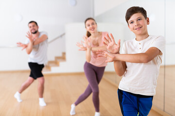 Cheerful preteen boy practicing vigorous dance movements in studio with his parents. Family bonding time and active lifestyle concept