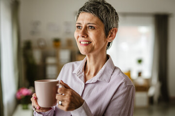 Portrait of mature woman stand and hold cup of coffee at home