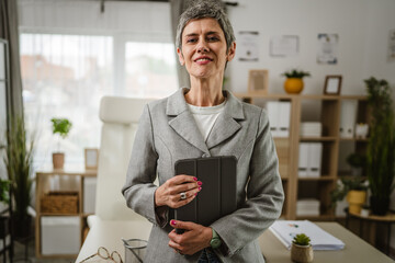 Portrait of mature caucasian woman stand and hold tablet at office