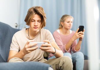 Portrait of teenage boy sitting on sofa at home interior with smartphone and looking at screen
